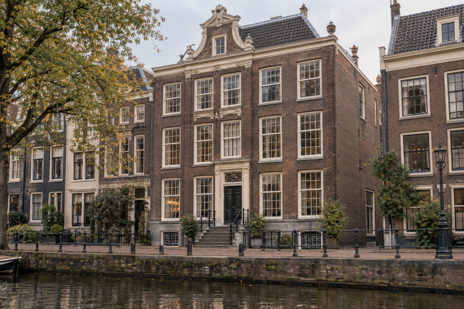 Karakteristiek bakstenen grachtenpand met hoge ramen en een stenen stoep aan het water.